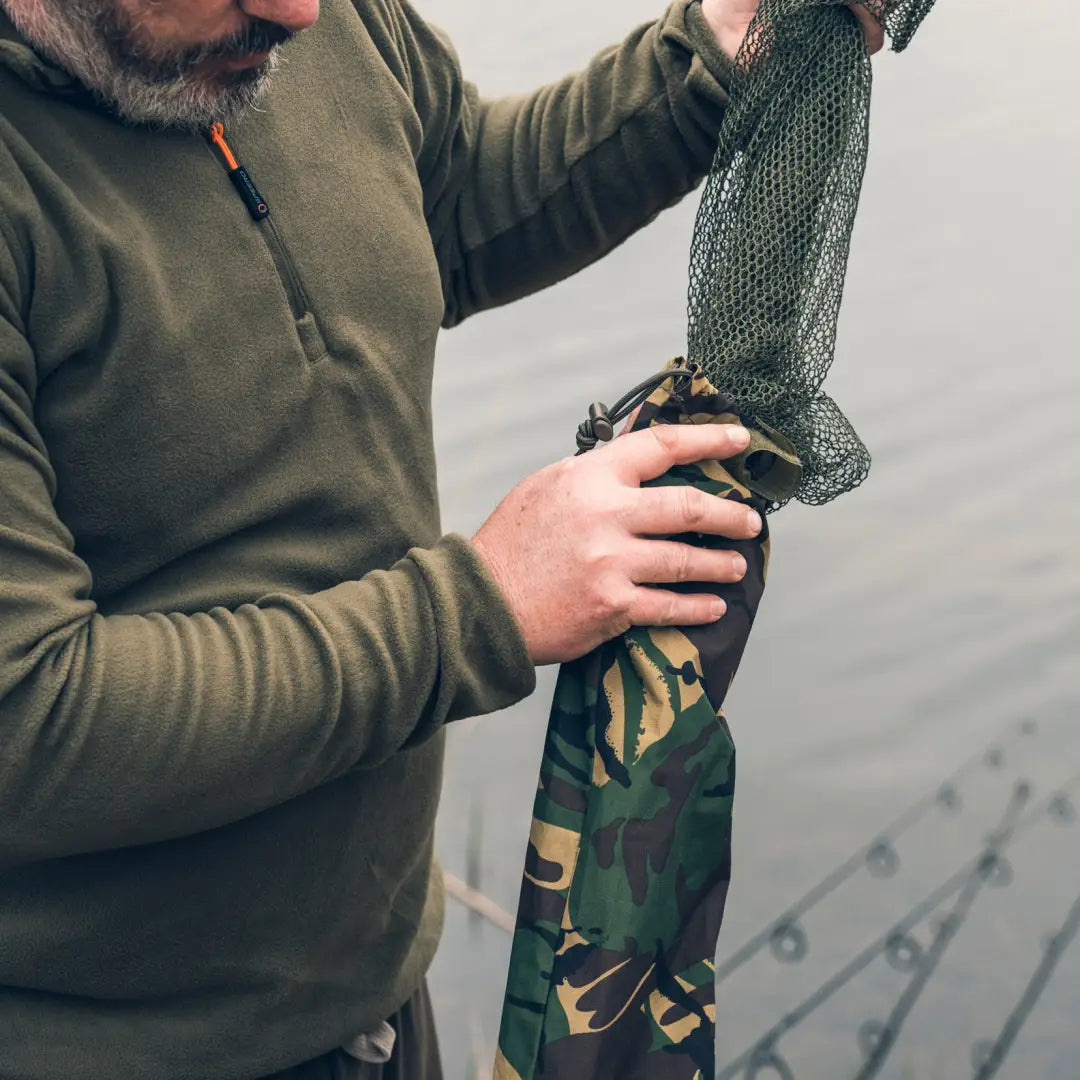 Person in outdoor gear holding a Speero Stink Sleeve with camouflage fishing net