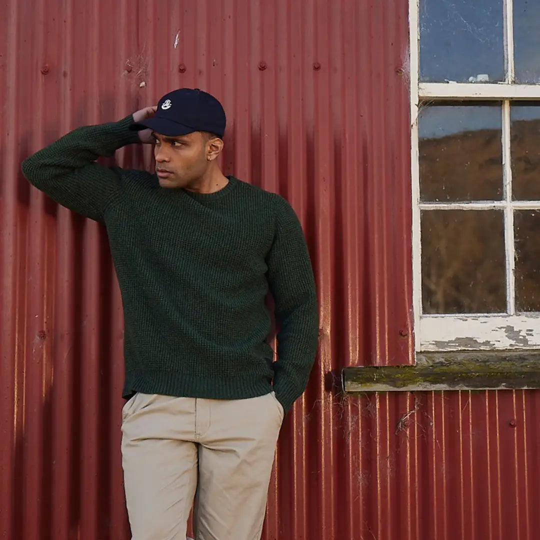 Man in a dark green waffle knit sweater and navy cap against a red wall, perfect for country clothing