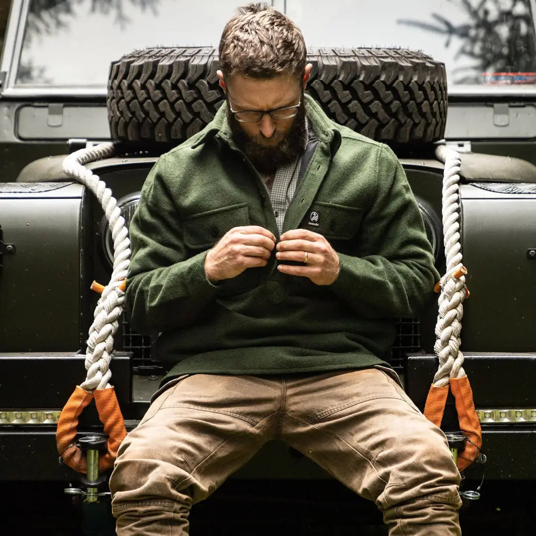 Man with a beard in a green jacket by a big tire showcasing Swanndri Ranger Extreme