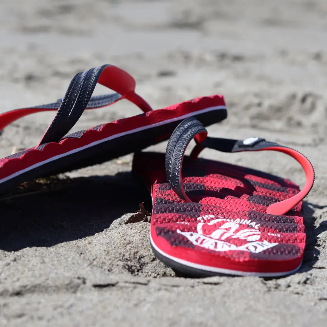 Red and black flip-flops on sand, perfect for outdoors and country clothing vibes