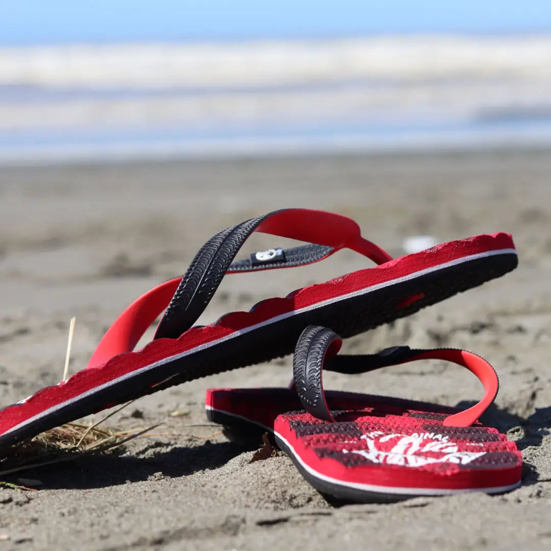 Pair of red and black Nike flip-flops on sand, perfect for outdoors and country clothing