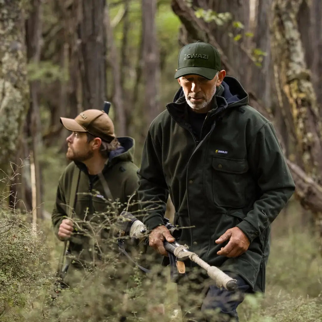 Two men hiking in the woods, one with a fishing rod and wearing a Swazi Legend Cap