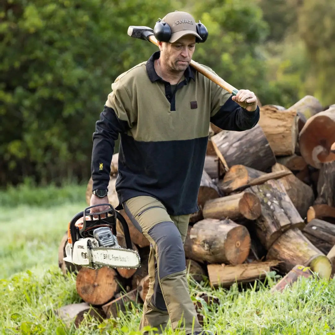 Man with chainsaw and axe next to wood, wearing a Swazi Rugger Jersey