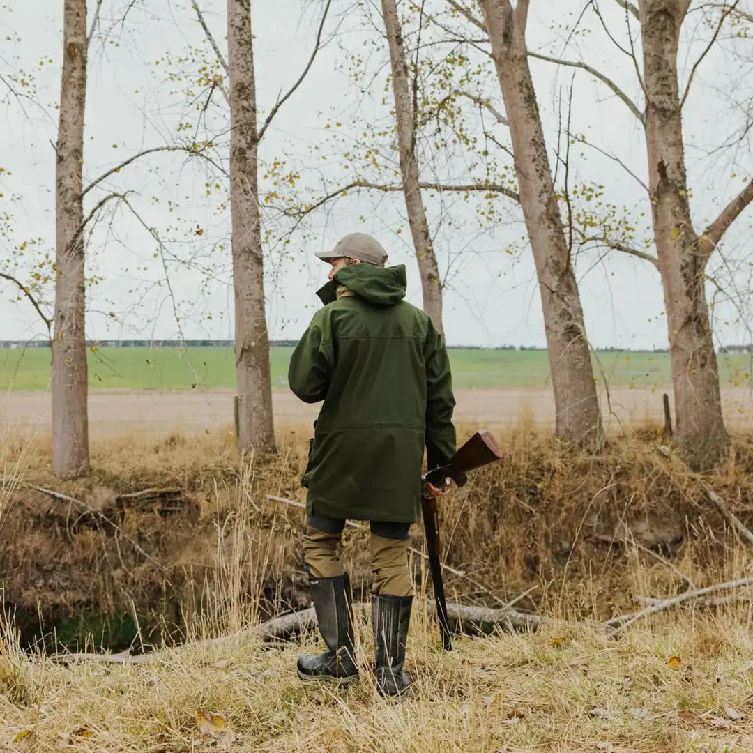 Hunter in green gear with rifle, showcasing stylish Wapiti coat among bare trees