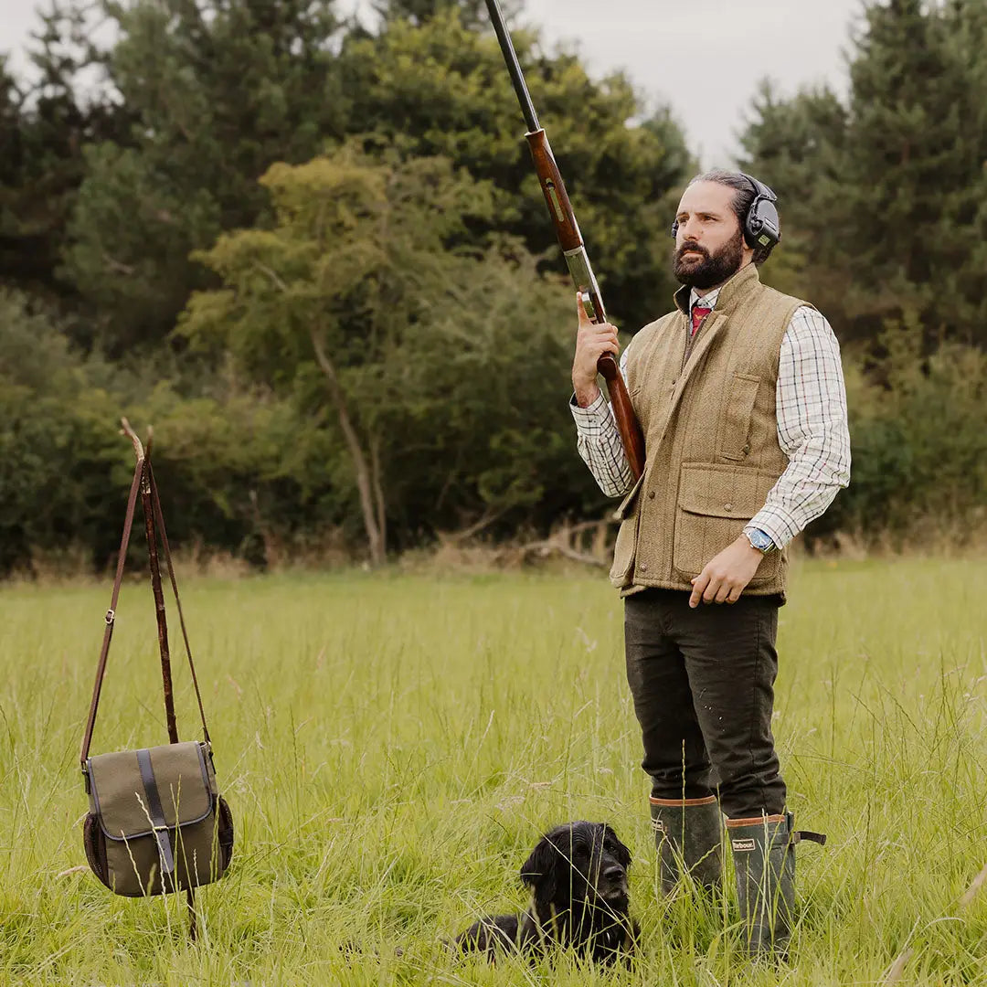 Man in tweed gilet with shotgun and dog in a grassy field for country clothing vibe