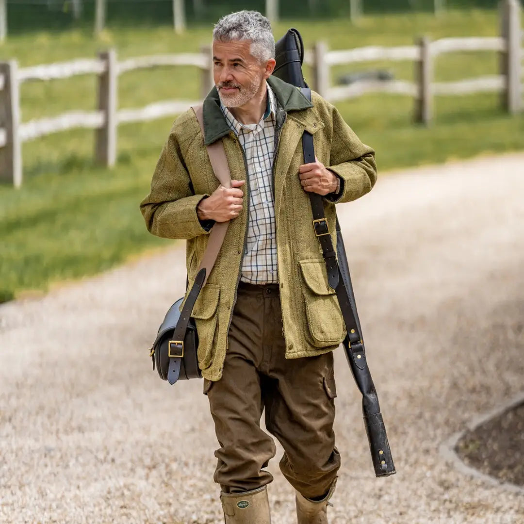 Man in hunting attire with a shotgun wearing a stylish Tweed Shooting Jacket